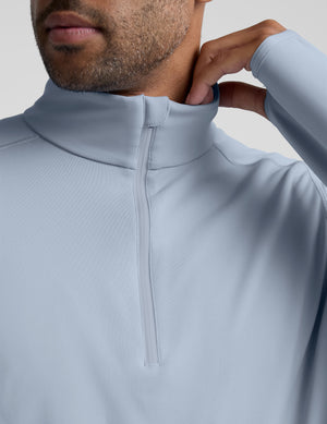 Man wearing a light blue quarter zip pullover and blue pants on a plain background. 