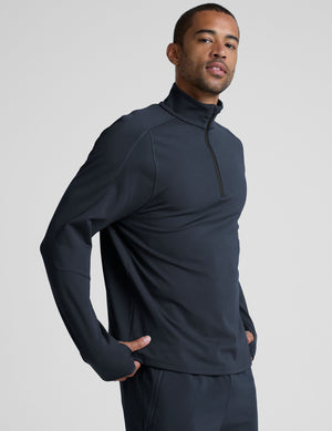 man wearing a dark blue quarter zip pullover against a plain background. 