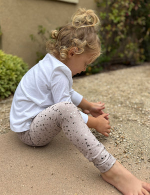 Child wearing a white long-sleeve shirt and patterned leggings standing outdoors.