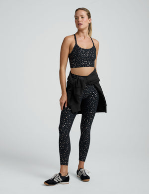 Woman wearing a black racerback cropped tank with a mini moons prints and leggings on a plain background. 