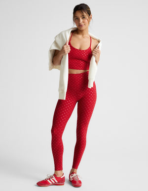 Woman wearing a red cropped tank with a hearts print and leggings with a plain background. 