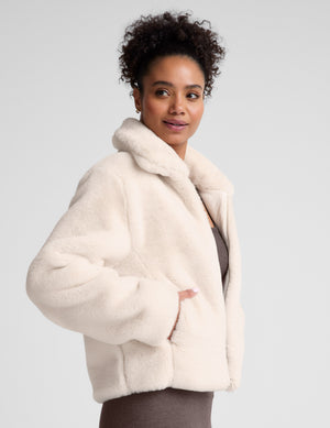 model wearing a light faux fur zip-up jacket against a plain background. 