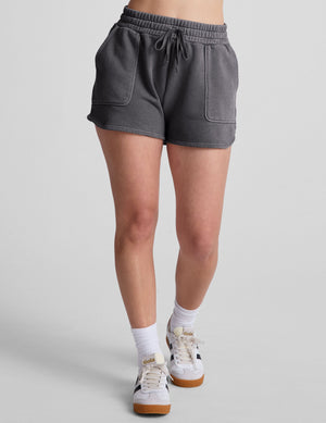 Gray Cali Short with drawstring waist, patch pockets, and dolphin hem, worn by a model in a neutral studio setting.