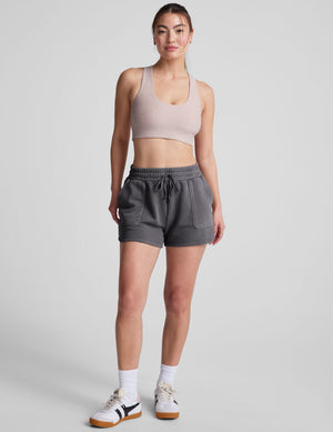 Model wearing dark gray Cali Short with drawstring waist and patch pockets. Relaxed dolphin hem shorts in soft terry fabric.