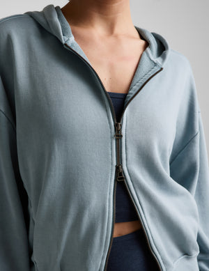 Woman wearing a blue zip-up jacket and blue biker shorts against a plain background. 