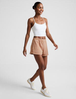 Woman wearing a white tank and brown fleece shorts against a plain background. 