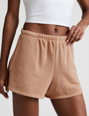 Woman wearing a white tank top and beige shorts on a light gray background. 