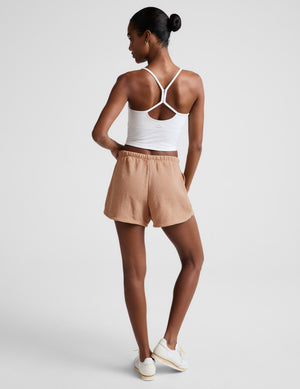 Woman wearing a white tank top and beige shorts on a light gray background. 