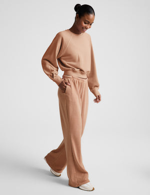 Woman wearing a beige sweatshirt and pants set on a plain background. 