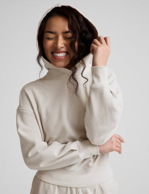 Woman wearing a white hoodie and pants against a plain background. 