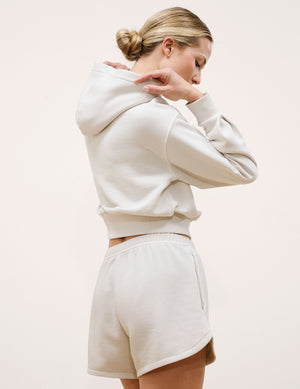 Woman wearing a white hoodie and shorts set against a plain background. 