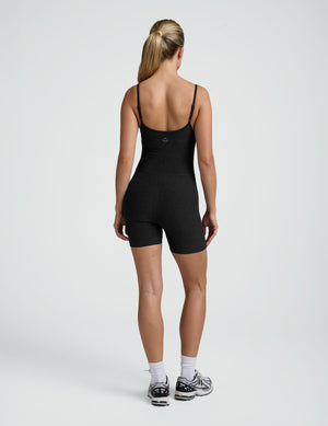 woman wearing a black biker bodysuit and sneakers on a plain background. 