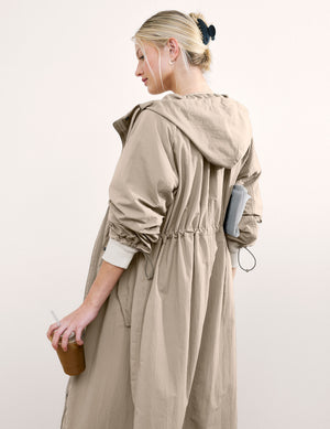 Woman wearing a beige trench coat against a white background. 
