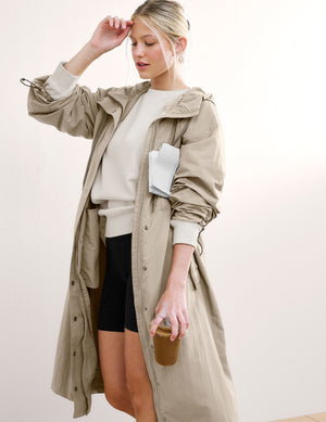 Woman wearing a beige trench coat against a white background. 