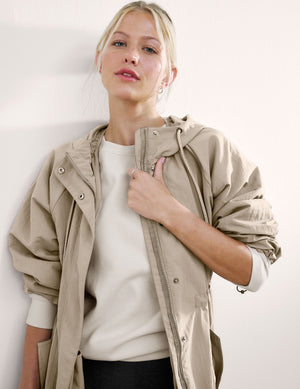 Woman wearing a beige trench coat against a white background. 