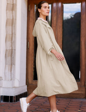 Woman in a beige trench coat walking. 