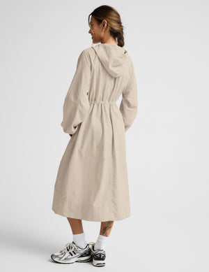 Woman in a beige trench coat against a plain background. 