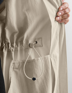 Woman in a beige trench coat against a plain background. 