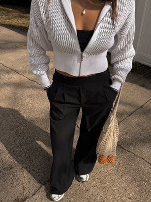Person wearing a white textured sweater and black pants on a concrete surface.