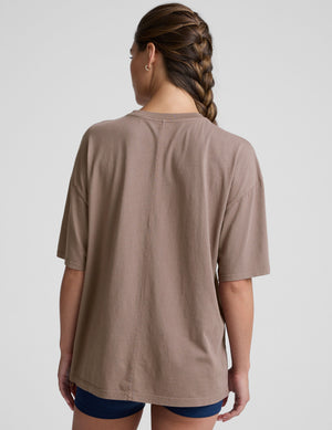 model wearing a brown oversized cotton t-shirt and navy shorts on a light gray background. 