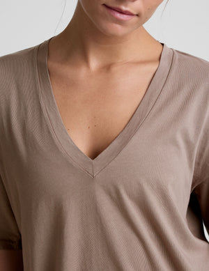 model wearing a brown oversized v-neck top and blue shorts on a plain background. 
