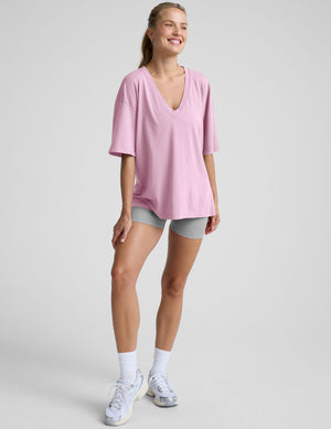 model wearing a pink oversized v-neck top and gray shorts on a plain background. 