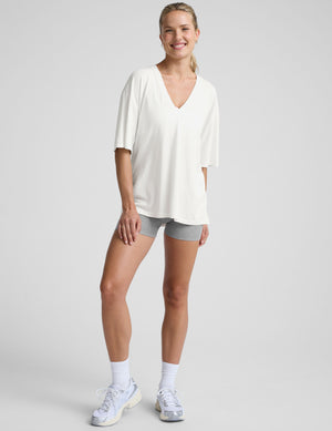 model wearing a white oversized V-neck top and gray shorts on a light background. 