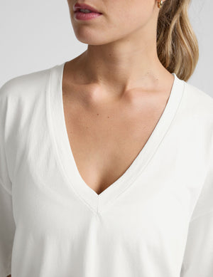 model wearing a white oversized V-neck top and gray shorts on a light background. 