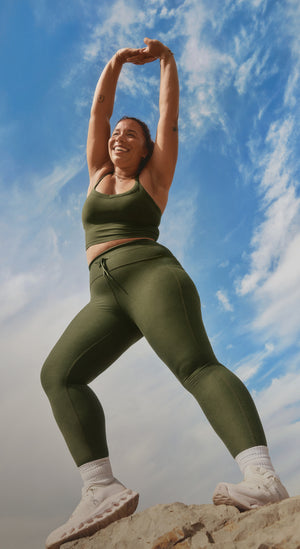 Person in green athletic wear stretching outdoors against a blue sky.