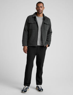 man wearing a dark gray shirt jacket over a gray shirt on a plain background. 
