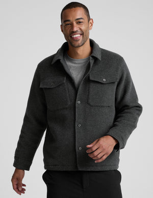 man wearing a dark gray shirt jacket over a gray shirt on a plain background. 