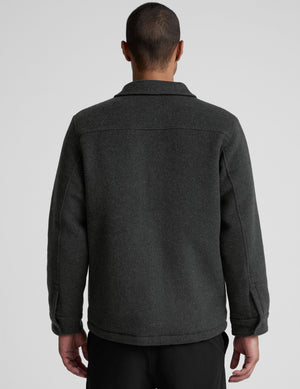 man wearing a dark gray shirt jacket over a gray shirt on a plain background. 