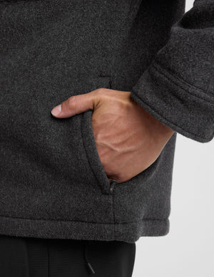 man wearing a dark gray shirt jacket over a gray shirt on a plain background. 