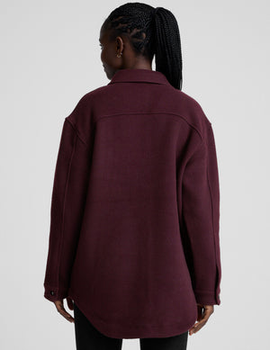 woman wearing a burgundy shirt jacket on a plain background. 