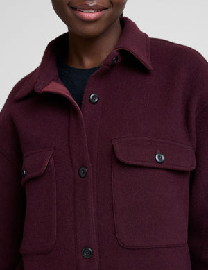 woman wearing a burgundy shirt jacket on a plain background. 