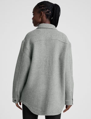 woman wearing a gray shirt jacket against a plain background. 