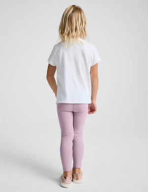 A child model shown from the back wearing a white short-sleeve t-shirt and dusty pink leggings, standing against a light gray studio background.