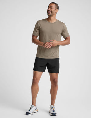 Man wearing a beige t-shirt and black shorts on a light gray background. 
