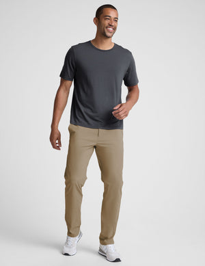 Man wearing a dark gray t-shirt and beige pants on a white background. 