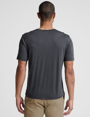 Man wearing a dark gray t-shirt and beige pants on a white background. 