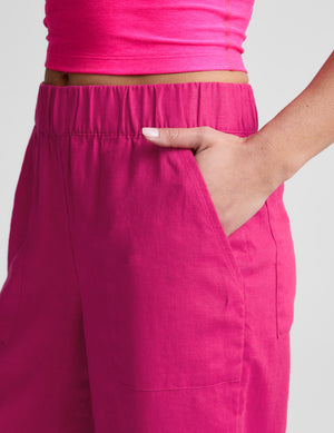 Woman wearing a pink tank and wide-leg linen pants against a plain background. 