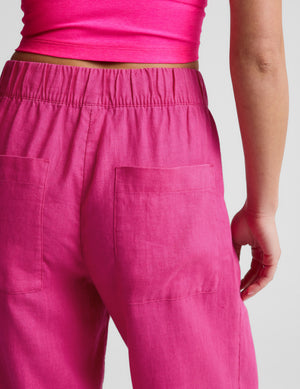 Woman wearing a pink tank and wide-leg linen pants against a plain background. 