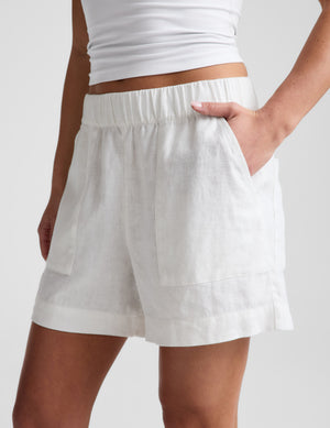 woman wearing a white tank top and shorts on a light gray background. 