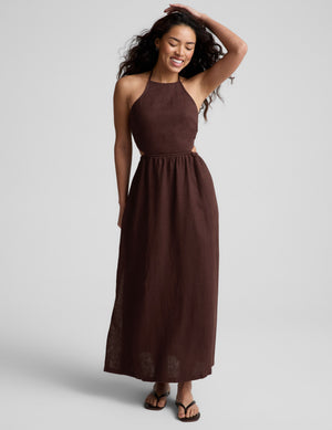 Woman wearing a brown halter neck midi dress on a plain background. 