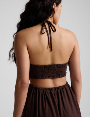 Woman wearing a brown halter neck midi dress on a plain background. 