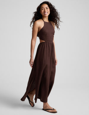 Woman wearing a brown halter neck midi dress on a plain background. 