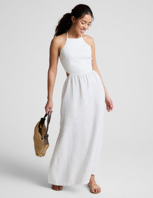 Woman wearing a white midi length halter dress against a plain background. 