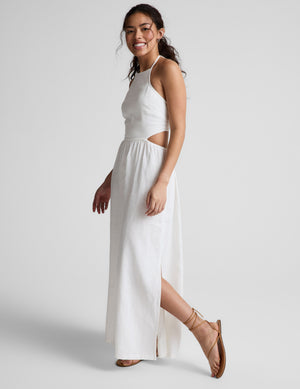 Woman wearing a white midi length halter dress against a plain background. 