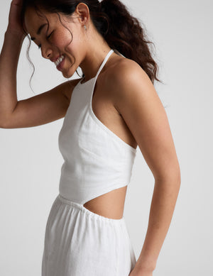 Woman wearing a white midi length halter dress against a plain background. 