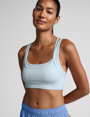 Woman wearing a light blue sports bra and shorts on a plain background. 